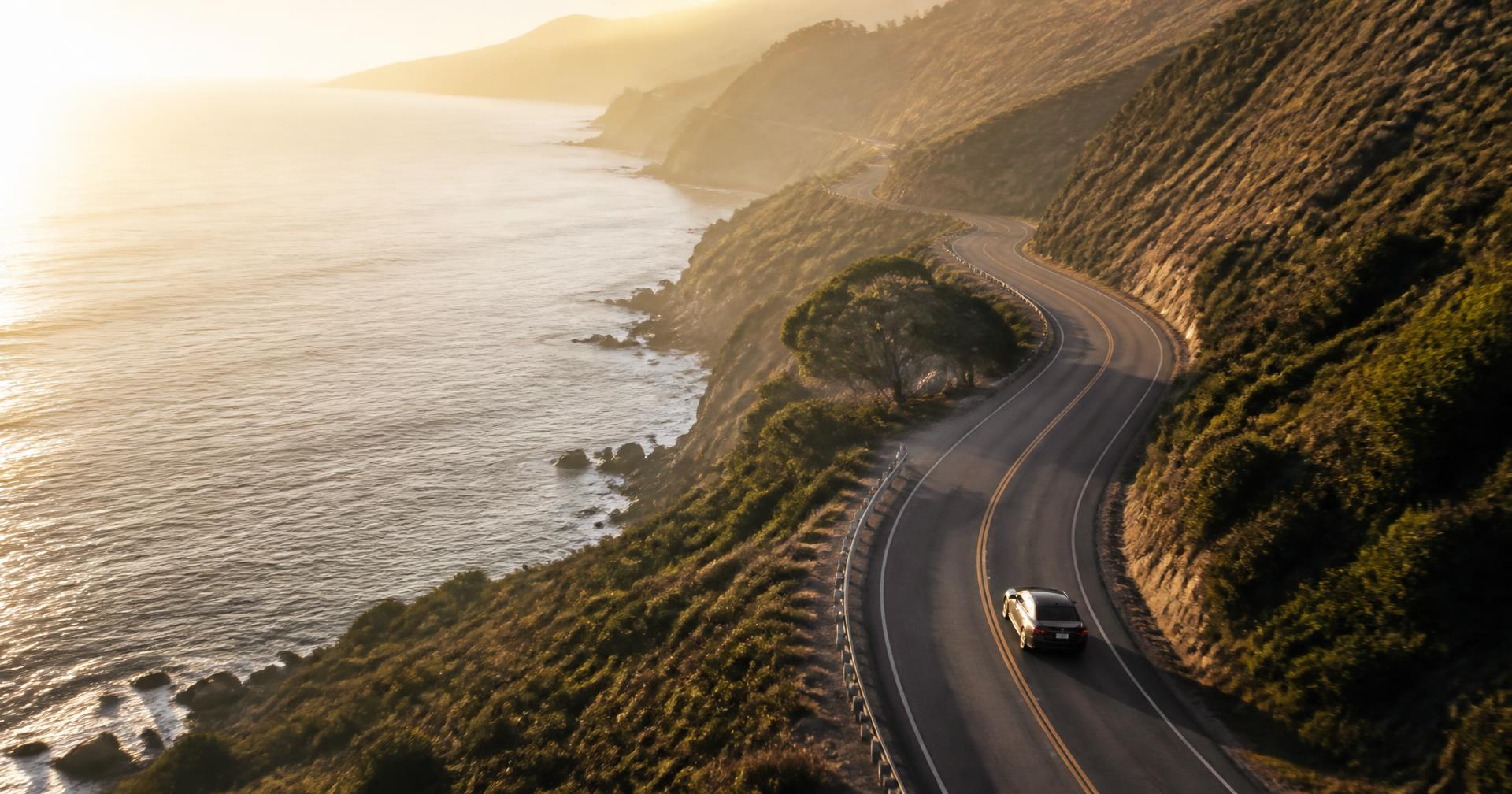 Luxury sedan on a sweeping coastal highway at golden hour
